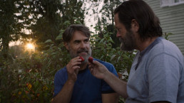 Plan sur Bill et Frank, cueillant des fraises dans leur jardin tandis que la lumière du soleil couchant perce à travers les branches des arbres derrière eux.