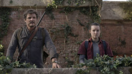 Extrait du dernier épisode de la saison 1 de The Last of Us (HBO). Joel et Ellie, incarnés par Pedro Pascal et Bella Ramsey, se tiennent debout, cote à cote, derrière un muret. On devine qu'ils sont en extérieur, sur un toit. Il fait jour et ils regardent quelque chose au loin, devant eux.