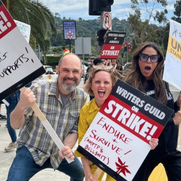 Photo de Craig Mazin, Halley Gross et Merle Dandridge manifestant lors de la grève des scénaristes ainsi que des acteurs et actrices à Hollywood. Chacun porte une pancarte avec un slogan différent dessus.